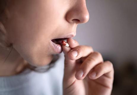 Closeup of person putting red and white capsule in mouth