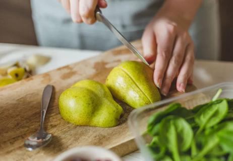 Person preparing pear to eat in a salad by slicing it lengthwise.