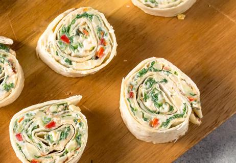 Cream cheese pinwheels with carrots, peppers and green onions diplayed on a wooden tray.