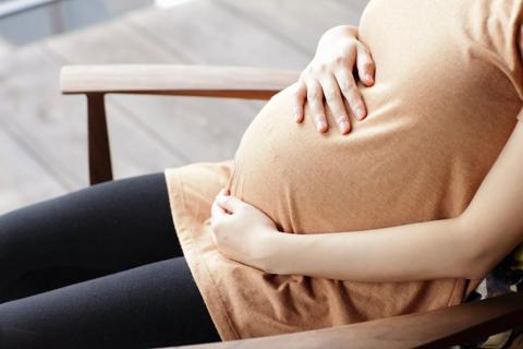 Closeup of person's seated torso with hands holding a pregnant belly
