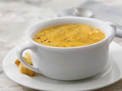 White crock of butternut, carrot and ginger soup on plate