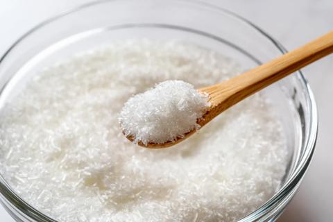 Wooden spoonful of monosodium glutamate over glass bowl full of MSG white crystals