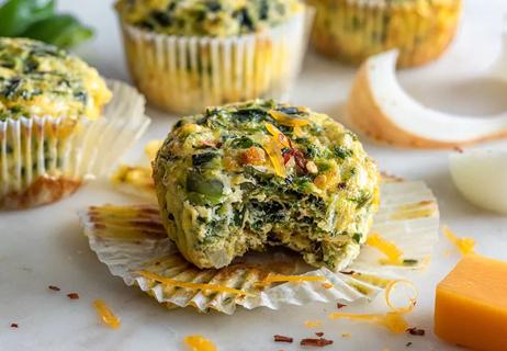 A yellow quiche muffin with green veggies with a bite out of it