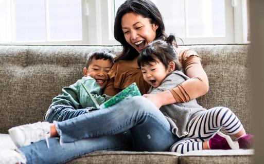 Caregiver laughing and reading to two happy kids on couch