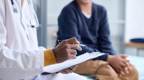 Healthcare provider holding clipboard, talking to patient sitting on exam table