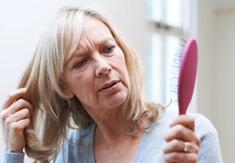 A woman concerned about hair loss stares at her hairbrush.