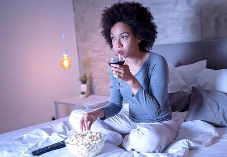 woman having wine and popcorn in bed