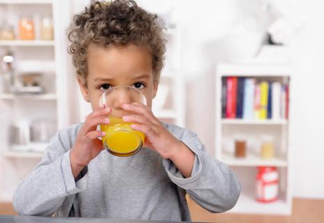 Toddler drinking orange juice from a glass