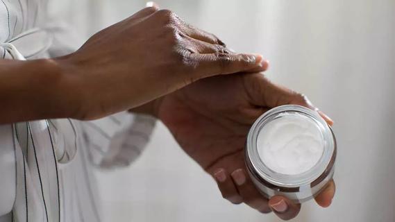 Close up of hand holding jar of moisturizer and applying to other hand