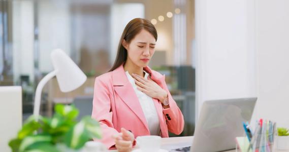 Person at desk at work, eyes closed in discomfort, hand at base of throat