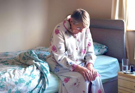 elderly woman sitting on bed experiencing aches and pains