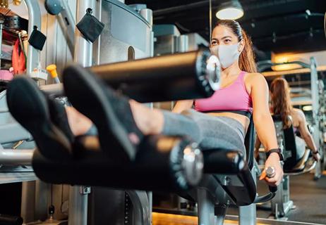 Female athlete training her legs in gym while wearing protective face mask