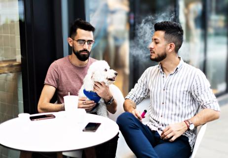 Young couple vaping at restaurant table outside.