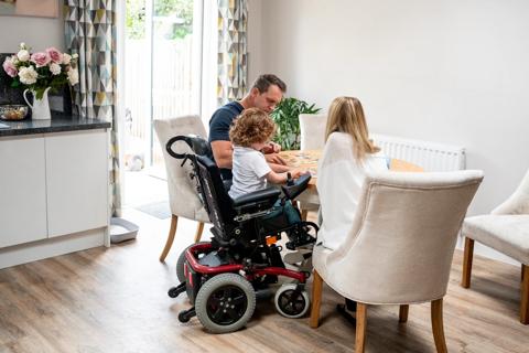 Family with young child in wheelchair putting together a puzzle at kitchen table