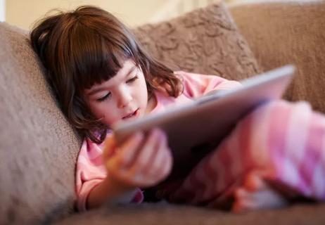 Child uses iPad while laying on couch