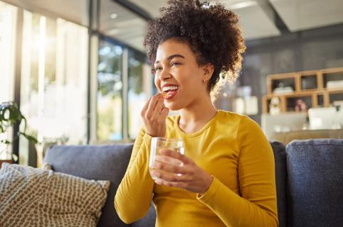 Young person smiling and holding a pill to their mouth while holding a glass of water in their other hand