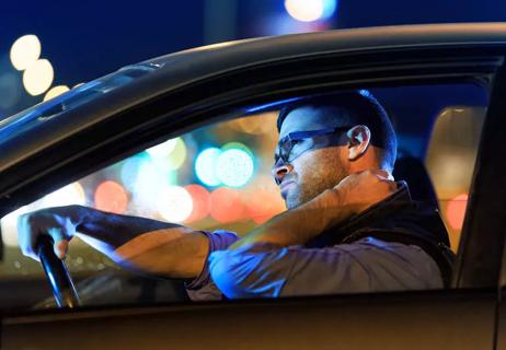 Man rubbing neck while driving car at night in traffic