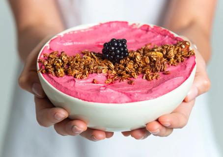 Hands holding a smoothie bowl with granola and a blackberry on top