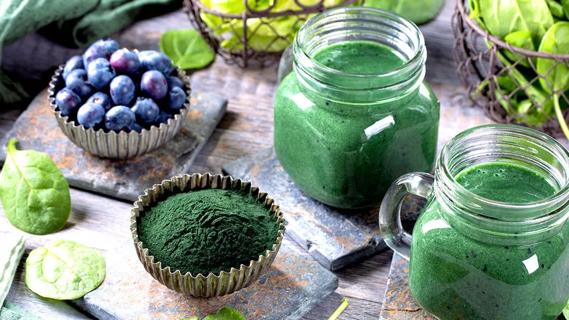 Powdered greens in a container, with powdered green smoothies and blueberries