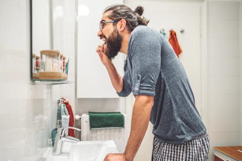 Bearded man brushing his teeth in home bathroom