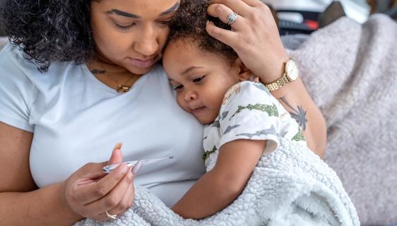 Caregiver holding thermometer and a sick child wrapped in blanket