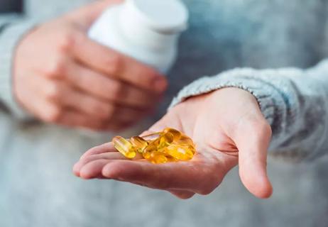 Person holding a handful of fish oil capsules after pouring them from a pill bottle.