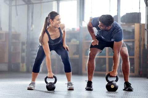 Woman and man lifting kettlebells at gym, smiling at each other