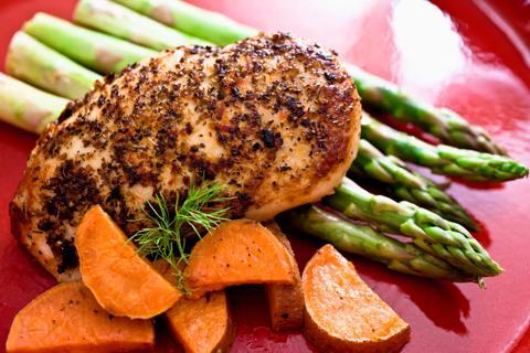 Grilled, seasoned chicken with asparagus and carrots on red plate