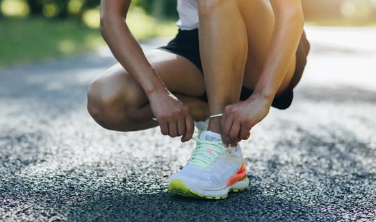 Person kneeled down tying running shoe on out door trail/track