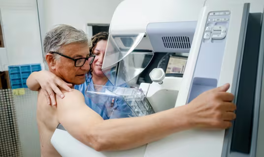 Older man getting a mammogram, with healthcare provider