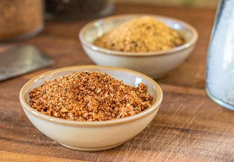 Two bowls of dry-rub spice blends on a wood table
