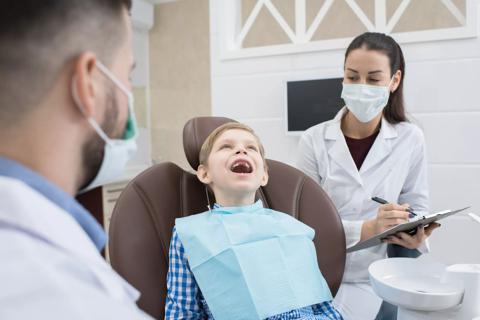 A child sitting in a dentist's chair with his mouth open