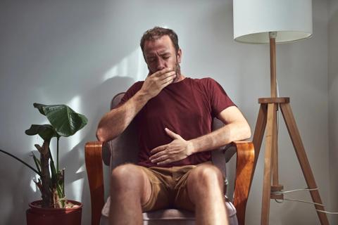 Person sitting in chair with hand on tummy and hand on mouth, burping