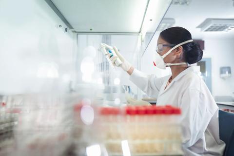 Scientist/lab tech in lab wearing mask and white coat working, with test tubes on counter