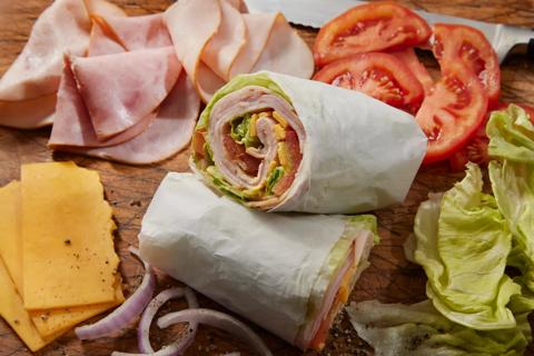 Turkey wrap cut in half on butcher board, with lettuce, tomato, cheese, onion