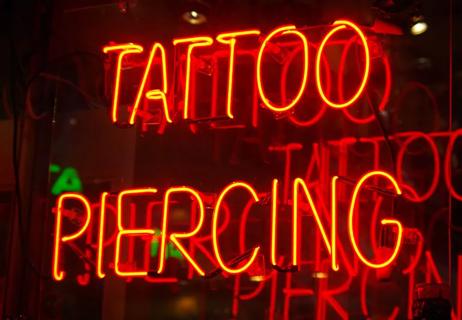 Neon sign in red that reads tattoo piercing.