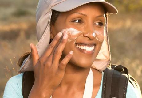 Hiker wearing hat applies sunscreen to face.