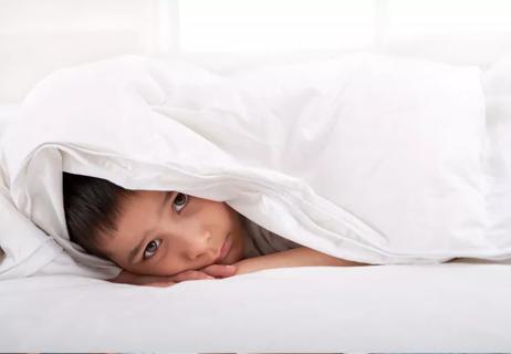 sad little boy peeking out of his bed covers