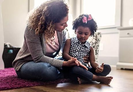 A woman sitting on the floor talking to a child.