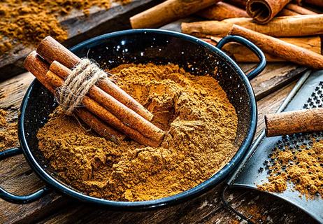 A bowl of cinnamon powder topped with a collection of cinnamon sticks