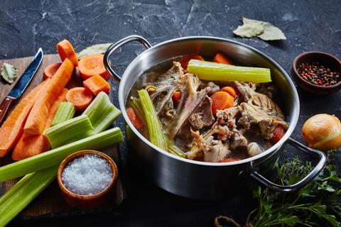 Steel pot cooking bone broth mixed with carrots and celery.