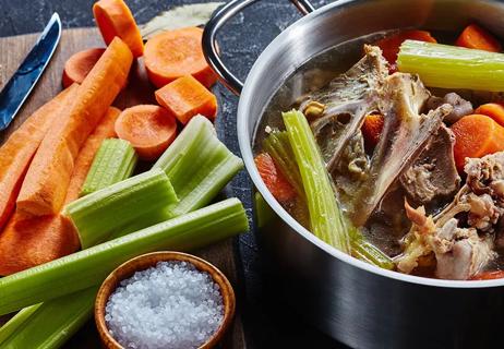Steel pot cooking bone broth mixed with carrots and celery.