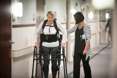 Physical therapist helping patient walk with a powered exoskeleton and walker