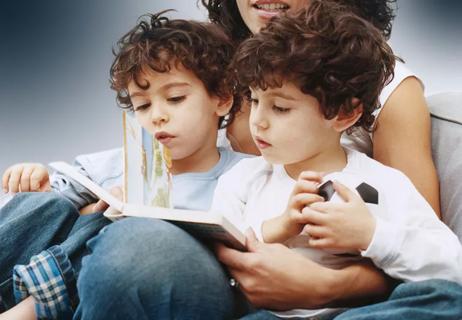 Parent reads to their twins while they sit in their lap and look at the picture book.