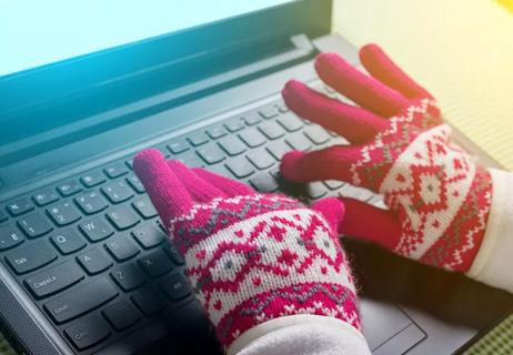 Goved hands typing on laptop in cold office environment
