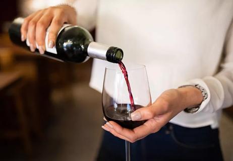 A person pouring red wine from a bottle into a wine glass