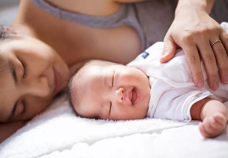 Mother lying down next to her sleeping newborn