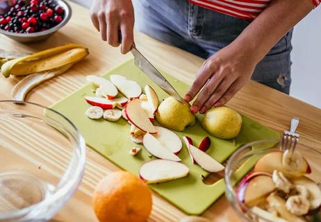 A person cutting apples and bananas on a cutting board.