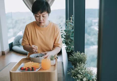 A person sits at a table eating strawberries, oranges and fruit juice.