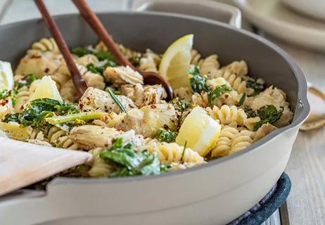 Closeup of a bowl of rotini with lemon slices and greens